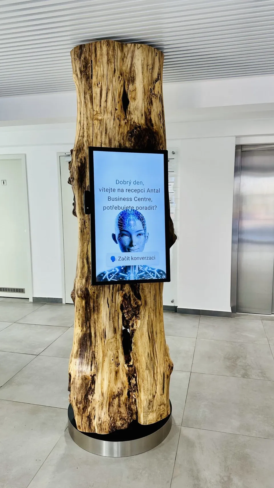 Terminál aReception s avatarem na obrazovce zasazený do kmene stromu v atriu Antal Business Centre
